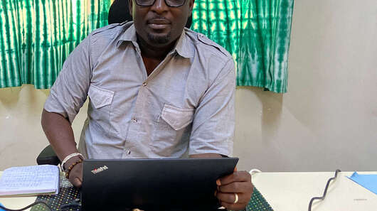 Ein Mann sitzt am Schreibtisch und schaut in die Kamera.