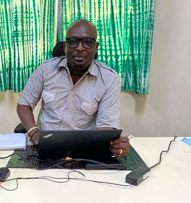 Ein Mann sitzt am Schreibtisch und schaut in die Kamera.