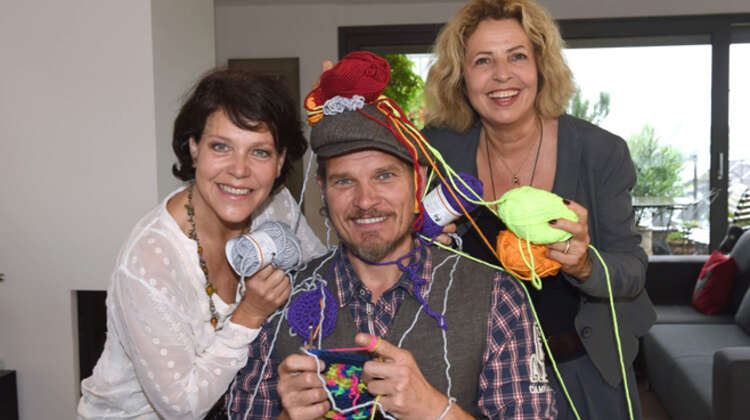 Götz Otto, Janina Hartwig und Michaela May schauen beim häkeln lachend in die Kamera.