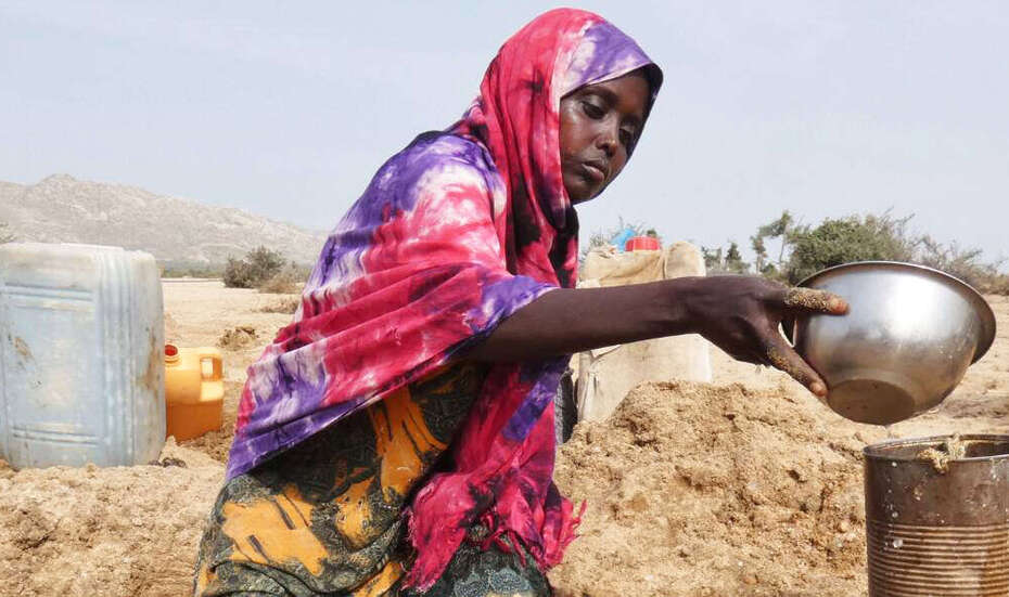 Eine Frau schöpft Wasser aus einem Loch im Boden.