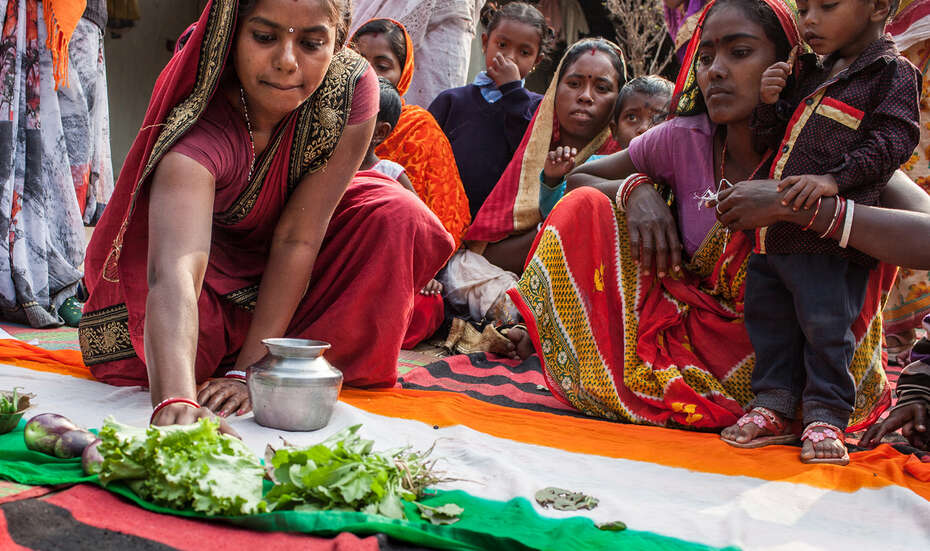 Eine Frau in einem Sari hockt auf dem Boden, vor ihr eine indische Flagge. Sie schiebt einen Salat auf den grünen Teil der Flagge.