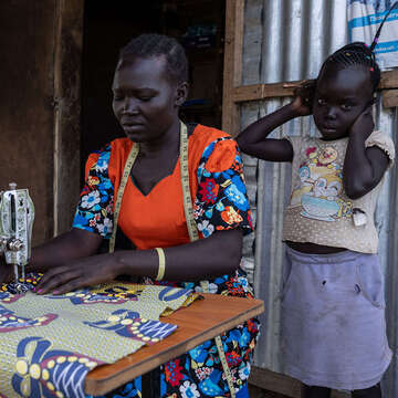 Frau in Uganda arbeitet an einer Nähmaschine, neben ihr ein Kind
