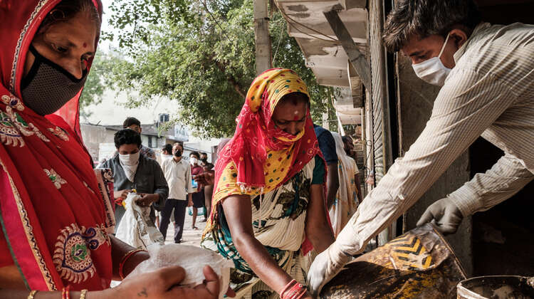 Frauen mit Maske verteilen Lebensmittel, Indien.