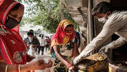 Frauen mit Maske verteilen Lebensmittel, Indien.