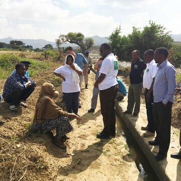 Mehrere Personen stehen und sitzen an einem Bewässerungskanal.