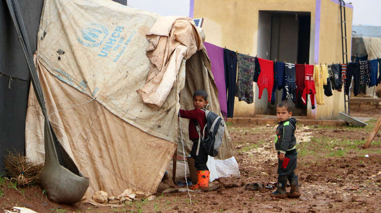2020-winterhilfe-syrien-kinder-camp-welthungerhilfe.JPG Zwei Kinder stehen vor einem Zelt in einem Flüchtlingscamp und schauen Richtung Kamera. An einer Leine ist Wäsche aufgehängt.