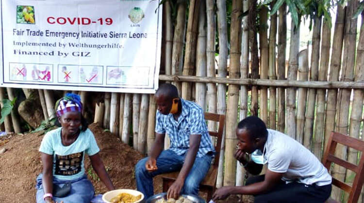 Kochkurse in Kailahun, Sierra Leone Eine Frau und zwei Männer sitzen an einem kleinen Tisch und essen.
