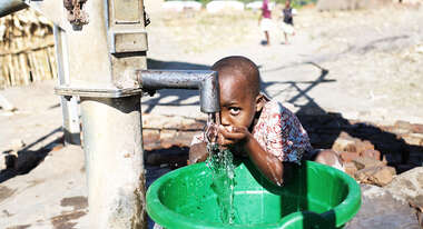 Ein Kind trinkt aus einem Brunnen.