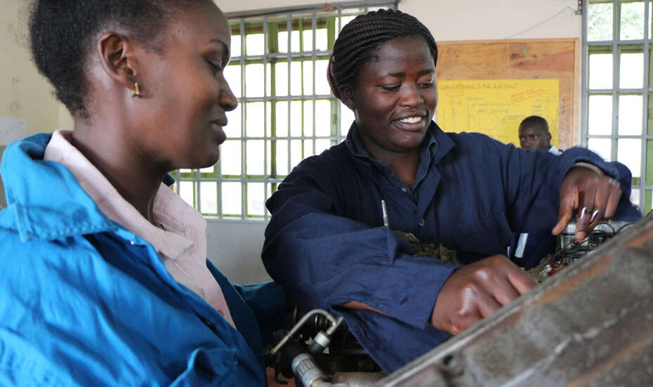 Zwei Frauen in blauen Anzügen reparieren ein Gerät.