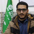 Portraitfoto von Welthungerhilfe-Mitarbeiter Adib Abokhors, der in Winterjacke vor einem Banner mit dem Logo der Welthungerhilfe sitzt