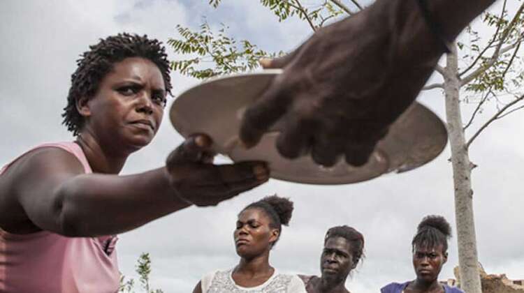 Eine Frau nimmt einen Teller mit Essen entgegen, Andere warten bereits.