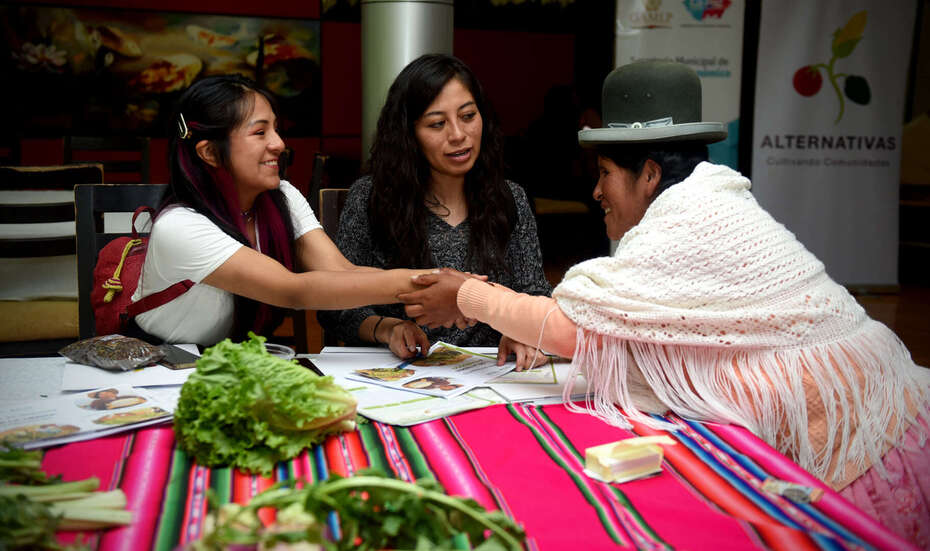 Drei Frauen unterhalten sich an einem Tisch, zwei schütteln die Hände