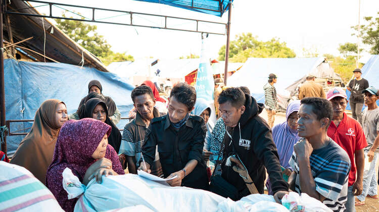 2019-nothilfe-tsunami-fluechtlingscamp-verteilung_C_acted.jpg Männer und Frauen stehen beisammen und schauen auf eine Liste.