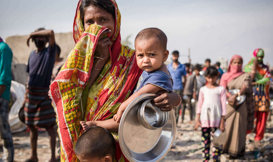 Eine Frau bedeckt mit einem Tuch Mund und Nase, sie hält ein Kind auf dem Arm und ein weiteres vor sich.