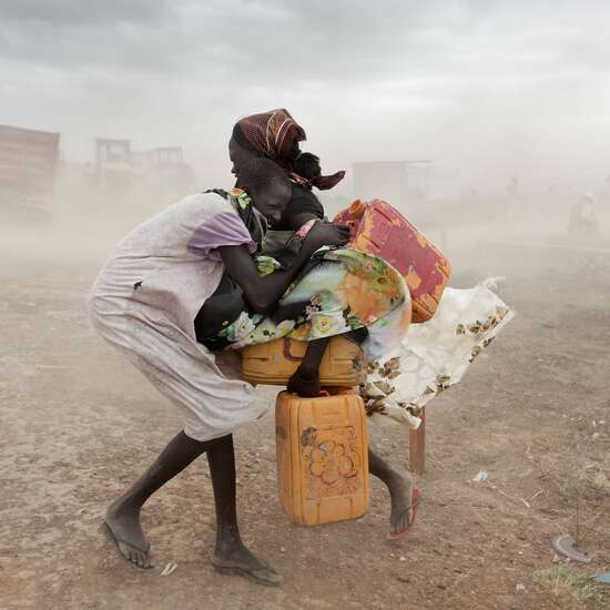 Zwei Mädchen mit Wasserkanistern versuchen sich vor einem starken Sandsturm zu schützen