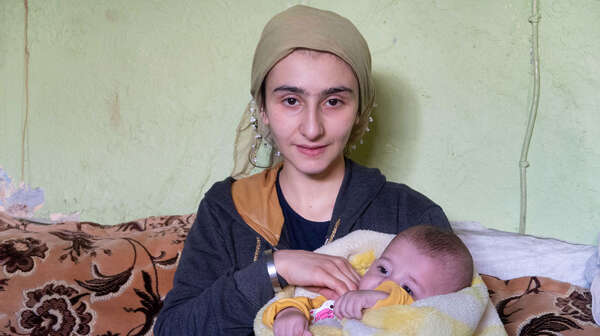 Eine Frau hält ein Baby im Arm und lächelt in die Kamera.