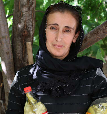 Eine Frau steht unter einem Baum, in der Hand hält sie zwei Flaschen mit Gewürzgurken, Türkei 2021.