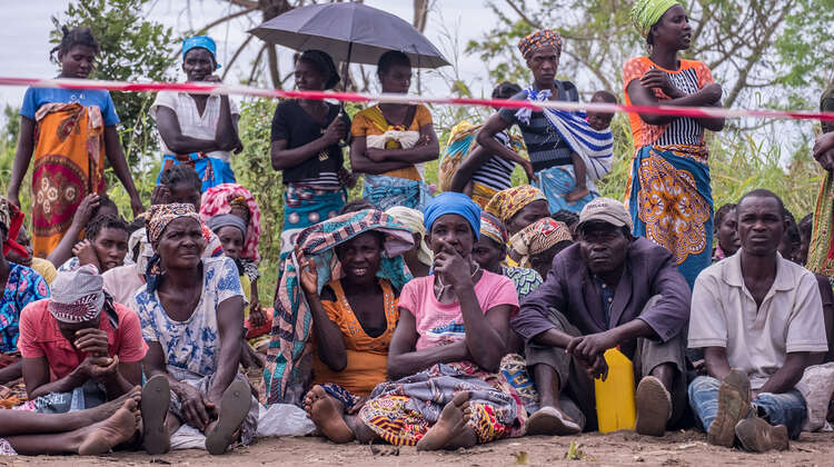 2019-nothilfe-nhamatanda-verteilung-mosambik-tommy-trenchard-concern.jpg Menschen warten stehend und sitzend hinter einer Absperrung.