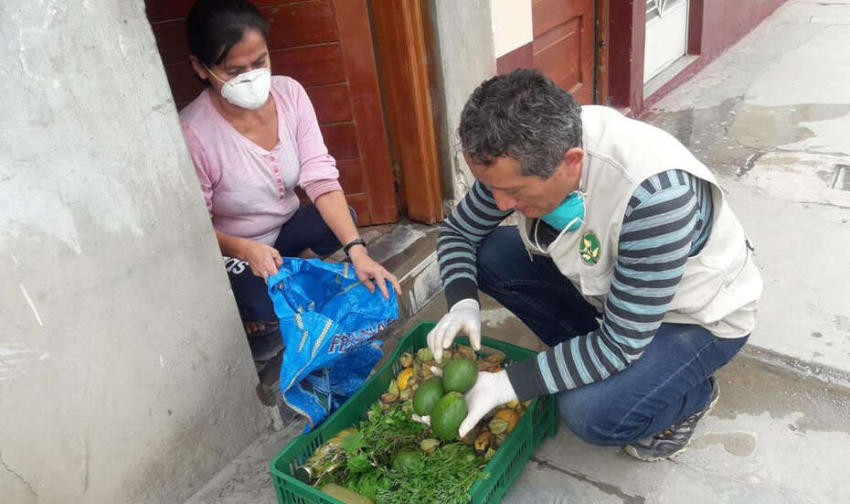 Eine Frau mit Maske kniet vor einem Korb mit Lebensmitteln, Peru 2021. 