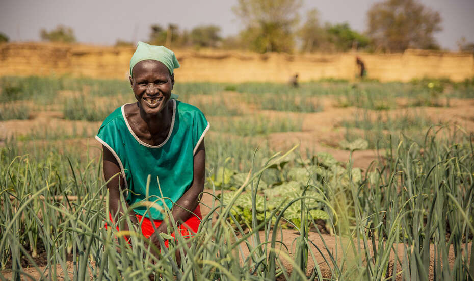 Eine Frau steht in einem Garten und lacht in die Kamera.