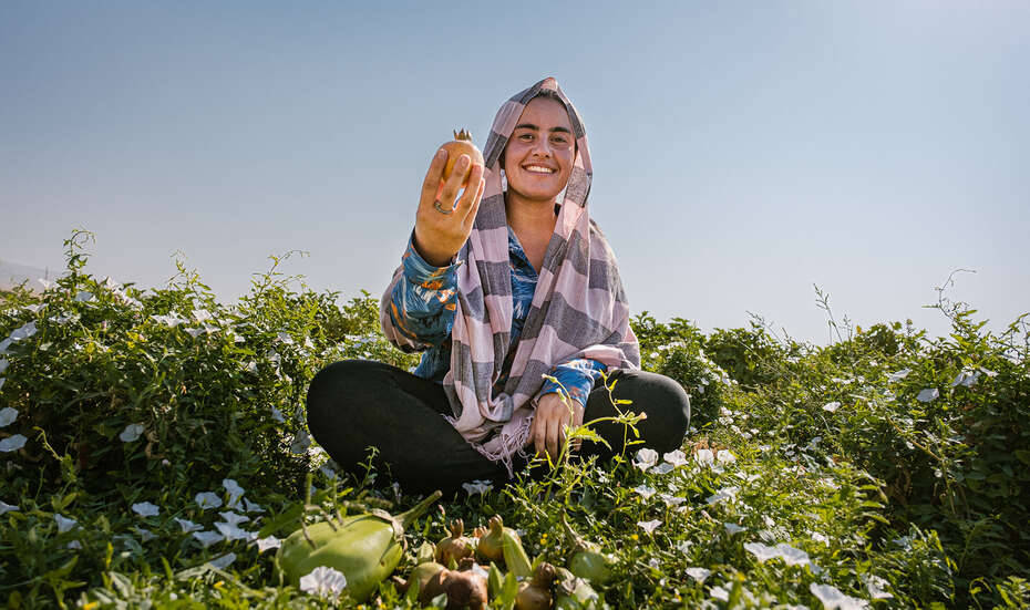 Frau sitzt im Feld und präsentiert stolz Früchte ihrer Ernte.