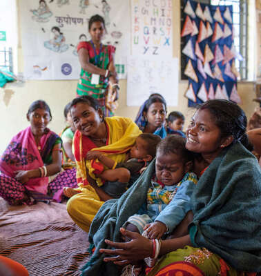 Frauen sitzen im Kreis und unterhalten sich. Manche haben Kinder auf dem Schoß.