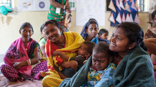 Frauen sitzen im Kreis und unterhalten sich. Manche haben Kinder auf dem Schoß.
