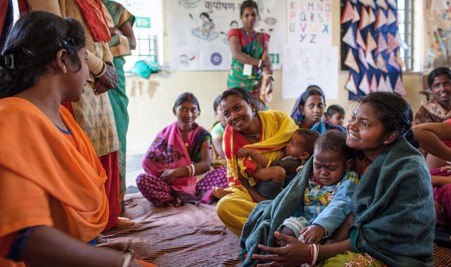 Frauen sitzen im Kreis und unterhalten sich. Manche haben Kinder auf dem Schoß.