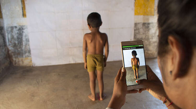 2020-indien-child-growth-monitor-smartphone-kind.jpg Eine Frau verwendet das Smartphone mit der Child Growth Monitor App um die Entwicklung eines Kindes zu messen, Indien 2020.