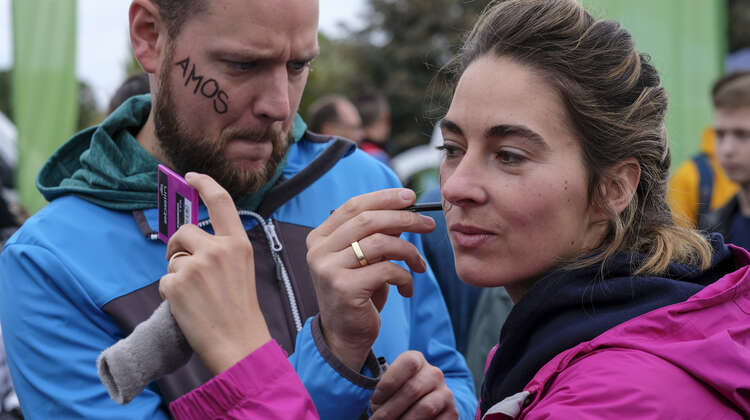 Eine Frau und eine Mann bemalen sich ihre Wangen.