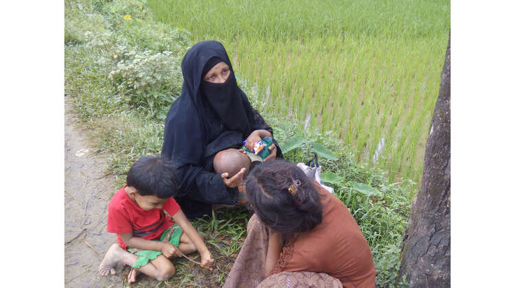 Zwei Frauen mit Baby und Kind sitzen am Straßenrand.