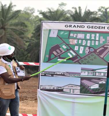 Ein Mann weist mit einem Zeigestock auf eine Tafel mit einem Bauplan.