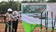Zwei Männer enthüllen eine Tafel mit dem Grundriss des geplanten Grand Gedeh County Hospital, Zwedru, Liberia, 2021 Zwei Männer enthüllen eine Tafel mit einem Bauplan.