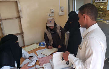 Hilfsarbeiter*innen stehen versammelt um einen Tisch und unterschreiben Dokumente.