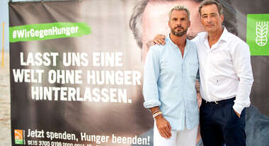 Die Schauspieler Stephan Luca und Jan Sosniok vor einem Plakat der Welthungerhilfe. Auf dem Plakat steht "Lasst uns eine Welt ohne Hunger hinterlassen".