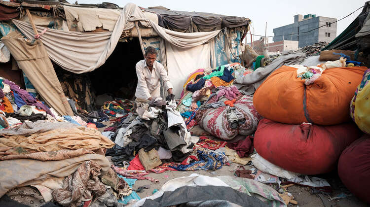 2020-coronavirus-obdachlosenunterkunft-arbeitsmigrant-innen-delhi-indien-c-florian-lang.jpg Ein Mann umgeben von Kleidungsstücken und alten Matratzen. Er sortiert Kleidung.