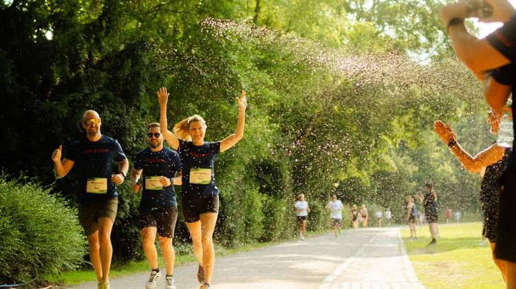 Läufer*innen werden von Zuschauern mit Wasser bespritzt und mit Handykameras aufgenommen