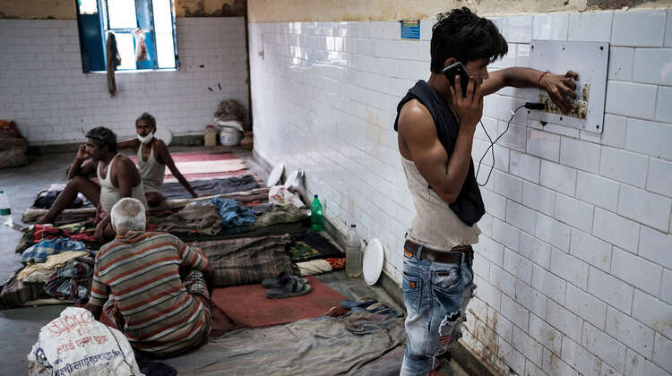 2020-coronavirus-slum-wanderarbeiter-delhi-indien-c-florian-lang.jpg Ein junger Mann steht an der Wand und telefoniert mit einem Handy.
