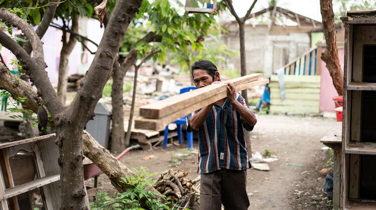 2019-nothilfe-tsunami-ueberlebender-indonesien_C_acted.jpg Ein Mann trägt zwei Holzlatten auf seiner Schulter.