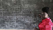 Bildung im Südsudan. Eine Lehrerin steht vor einer mit Kreide beschriebenen Schultafel