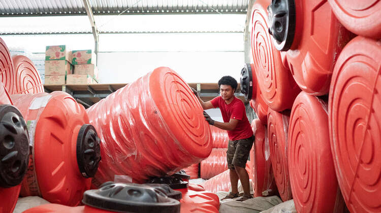 2019-nothilfe-tsunami-nothelfer-wassertanks_C_acted.jpg Ein Mann inmitten von großen roten Wassertanks.