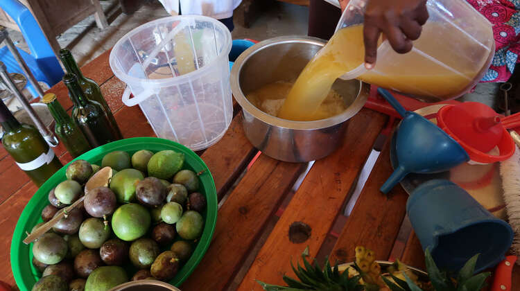 Ein Tisch mit einer Schüssel voller Maracujas, daneben schüttet jemand Saft in einen Topf.