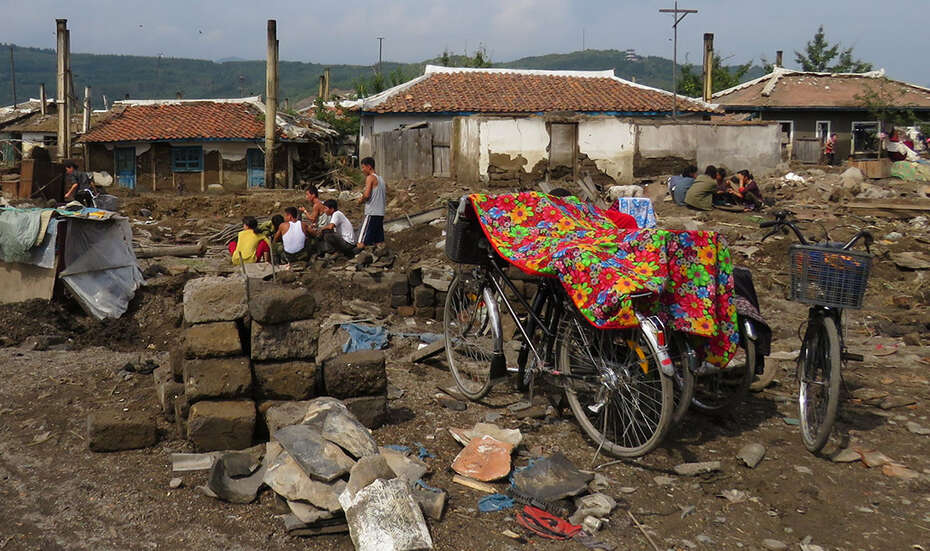 Menschengruppen sitzen in den Trümmern ihrer Häuser.