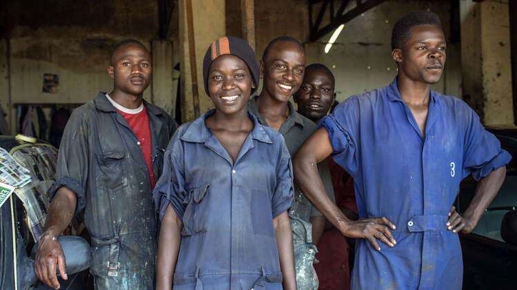 2017-skill-up-auszubildende-uganda_C_Imke-Lass-16-9.jpg Eine Gruppe junger Menschen in blauen Arbeitsanzügen schauen lächelnd in die Kamera