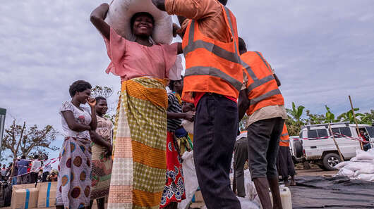Eine Frau bekommt von einem Mann in Sicherheitsweste Säcke und Pakete.