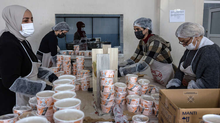 Frauen in Arbeitskleidung verpacken frisch gekochte Mahlzeiten in Transportboxen.