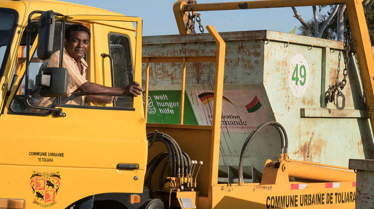Ein Fahrer schaut aus dem Fenster eines LKW mit Müllcontainer.