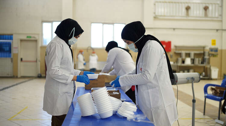 Frauen stehen an einem Tisch und füllen Transportboxen mit Lebensmitteln