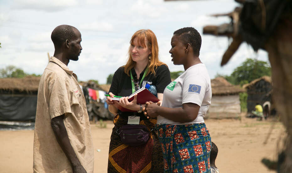 Zwei Frauen unterhalten sich mit einem Mann, eine hält ein Notizbuch in der Hand.