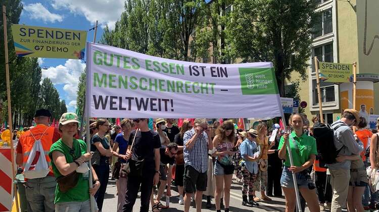 2022-G7-Demo-WHH-Banner_c_Welthungerhilfe.jpg Demonstrierende halten ein Banner hoch auf dem steht: Gutes Essen ist ein Menschenrecht - weltweit
